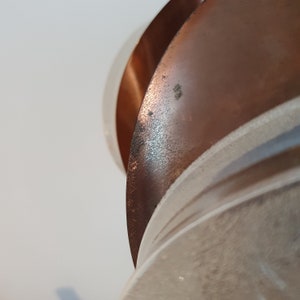 May include: Close-up of a copper-coloured metal sculpture with a white background. The sculpture is made of several curved pieces of metal that are layered on top of each other.