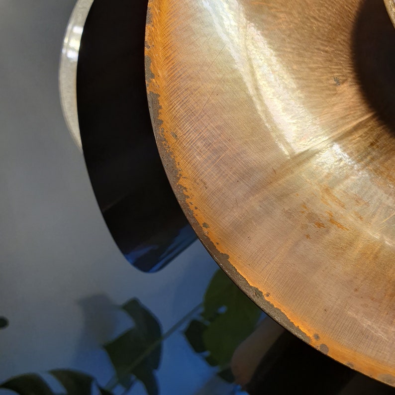 May include: Close-up of a copper-coloured metal bowl with a slightly rusted edge. The bowl is curved and has a shiny, reflective surface.