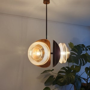 May include: A modern, mid-century style pendant light fixture with three frosted glass shades. The shades are suspended from a black metal rod and have a brass finish. The light fixture is illuminated with warm white light bulbs.