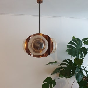 May include: A copper and glass pendant light fixture with multiple circular shades. The shades are translucent and have a frosted glass finish. The light fixture is suspended from the ceiling by a thin black cord.