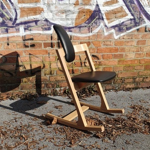 Peut inclure: Une chaise berçante en bois avec un siège en cuir noir. La chaise est devant un mur de briques avec des graffitis.