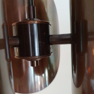 May include: A close-up of a brown metal lamp with a black metal arm and a round, copper-coloured base. The lamp has a unique design with a series of overlapping, curved shades.