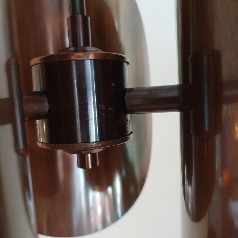 May include: A close-up of a brown metal lamp with a black metal arm and a round, copper-coloured base. The lamp has a unique design with a series of overlapping, curved shades.