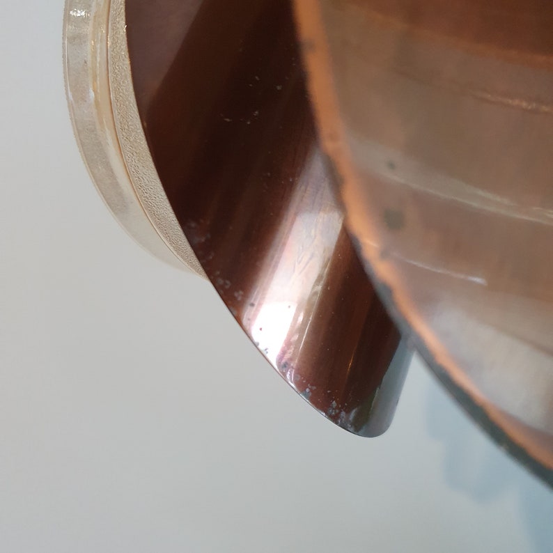 May include: Close-up of a copper-coloured metal lampshade with a white plastic base.