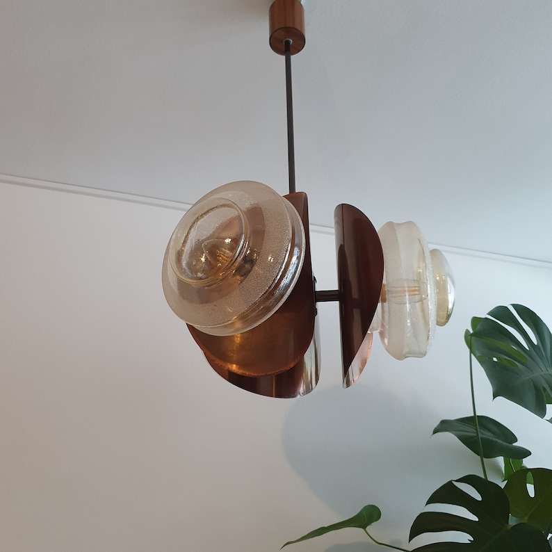 May include: A mid-century modern pendant light fitting with three glass shades and a copper finish. The shades are round and have a textured surface. The fitting is suspended from a black cord.