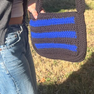 May include: A black and blue crocheted crossbody bag with a striped pattern. The bag has a long strap and is made of yarn.