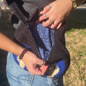 May include: A black crocheted tote bag with a blue and white star patterned lining. The bag has a blue and white crocheted design on the bottom.