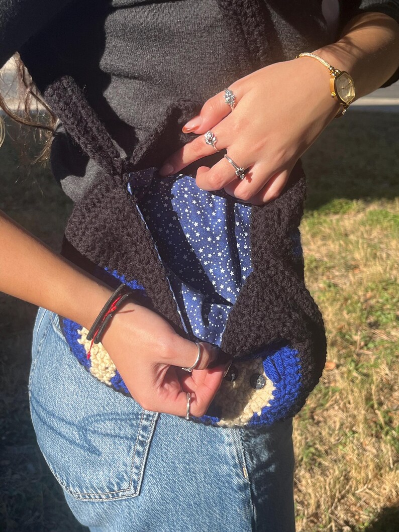 May include: A black crocheted tote bag with a blue and white star patterned lining. The bag has a blue and white crocheted design on the bottom.