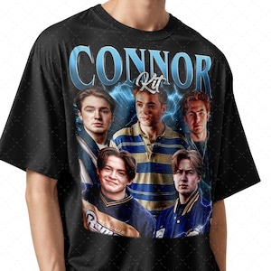 May include: Black t-shirt featuring a graphic of five young men with the name "CONNOR" in blue, stylized text. The word "Kit" is above the central figure. The background includes blue lightning bolts.