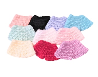 May include: A collection of ten small, handmade crochet skirts in various solid colors including black, white, light blue, pink, red, lavender, and cream. Each skirt features a flared, ruffled silhouette with a visible textured yarn stitch.