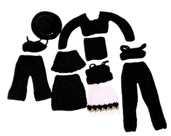 May include: A collection of miniature doll clothing items including a black hat, a black long-sleeved top, black pants, a black skirt, a black top, and a pink skirt with a black and gold trim. Each piece is crafted from black or pink yarn.