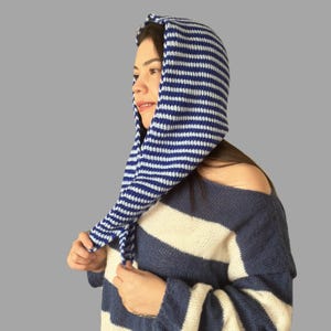 May include: A blue and white striped knit hood. The hood is worn over the head and has long, dangling ends. The person in the image is also wearing a blue and white striped sweater.