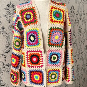 May include: A colorful, open-front crochet cardigan. The jacket features a patchwork design with vibrant squares in shades of red, yellow, blue, green, and pink, set against a cream-colored background. The sleeves are long and flared.