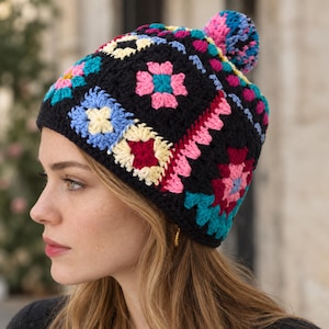 Può includere: Un berretto all'uncinetto caratterizzato da un motivo a piastrelle granny colorate con filati nero, rosa, azzurro, giallo e rosso scuro. Il berretto è sormontato da un pon-pon multicolore abbinato e realizzato con motivi quadrati uniti insieme.
