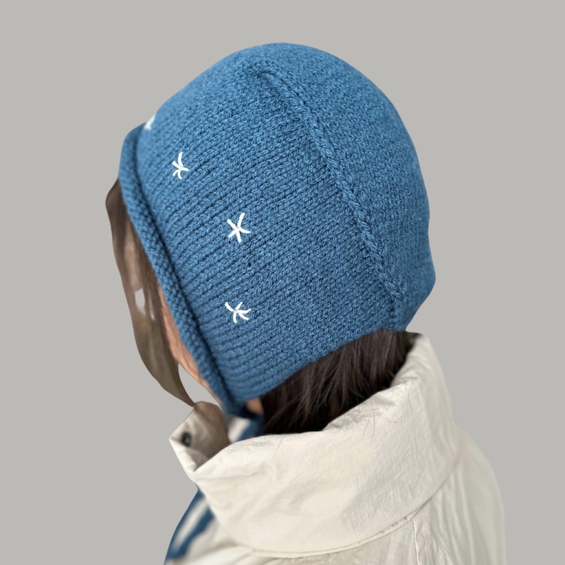 May include: A blue knitted beanie with white embroidered stars. The beanie has a fold-over brim and is made of a soft, warm material.