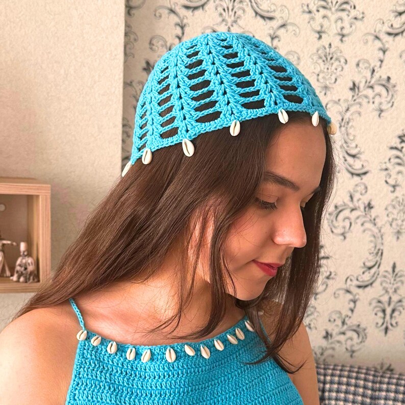 May include: A light blue crochet hat with a white shell trim. The hat is worn by a person with long brown hair.