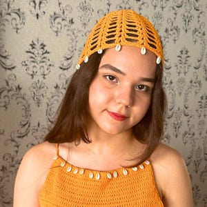 May include: A crocheted hat in a bright yellow color with white shell accents. The hat has a wide brim and a loose fit.