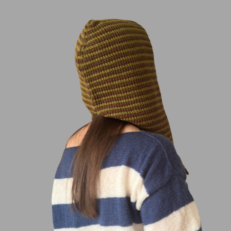 May include: A hooded hat with a striped pattern in shades of brown and olive green. The hat is worn over a blue and white striped sweater. The hat's design is visible from the back, showcasing its texture and shape.