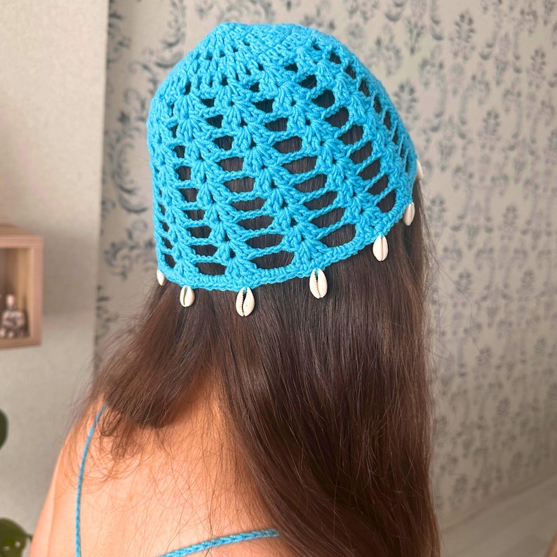 May include: A blue crocheted hat with a white shell trim. The hat is worn on a person with long brown hair.