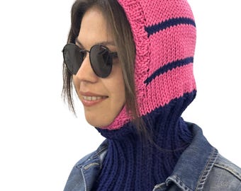 May include: A pink and navy blue knitted balaclava. The hood is pink with navy blue stripes, and the neck warmer is navy blue. The balaclava is designed to cover the head, neck, and face, leaving only the eyes visible.