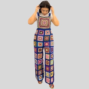 Könnte beinhalten: Ein blauer Häkel-Overall mit quadratischem Muster. Der Overall hat ein Lätzchen-Oberteil und weite Beine mit einer Vielzahl farbenfroher Quadrate. Das Kleidungsstück ist handgefertigt und hat einen Bohemian-Stil.