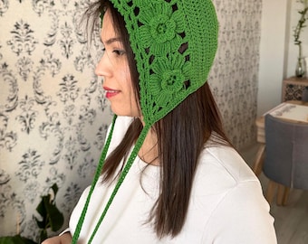 May include: A green crocheted hat with a flower design and long ties. The hat is made with a delicate stitch and has a vintage style.
