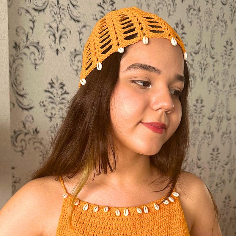 May include: A crocheted hat with a shell trim in a bright yellow color. The hat is worn by a person with long brown hair.