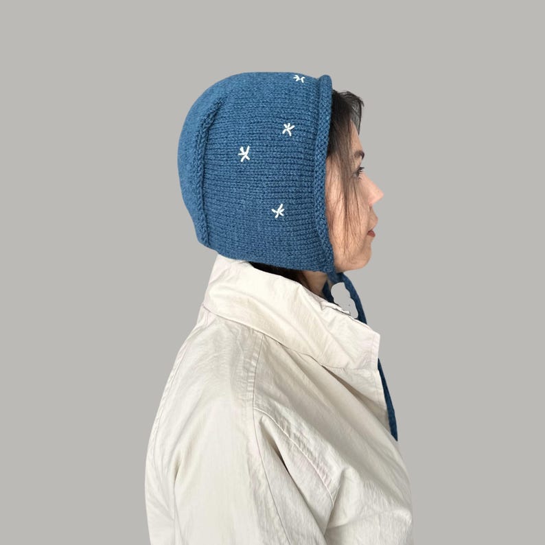 May include: A blue knitted hat with white embroidered stars. The hat has a long tie that can be tied under the chin.