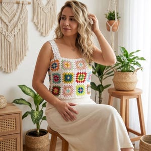 May include: A white crochet top with a colorful square pattern and white straps. The top is paired with a cream-colored skirt. The top is a handmade item, perfect for summer or a casual look.