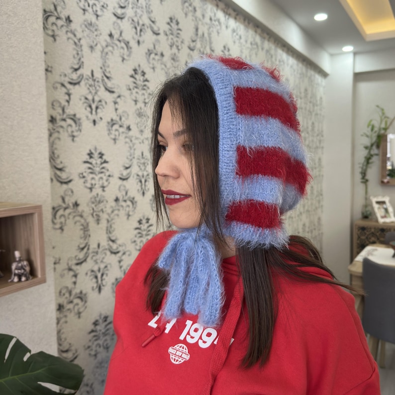 May include: A blue and red striped knit hat with a long, fluffy scarf. The hat has a pointed top and covers the ears. The scarf is tied around the neck.