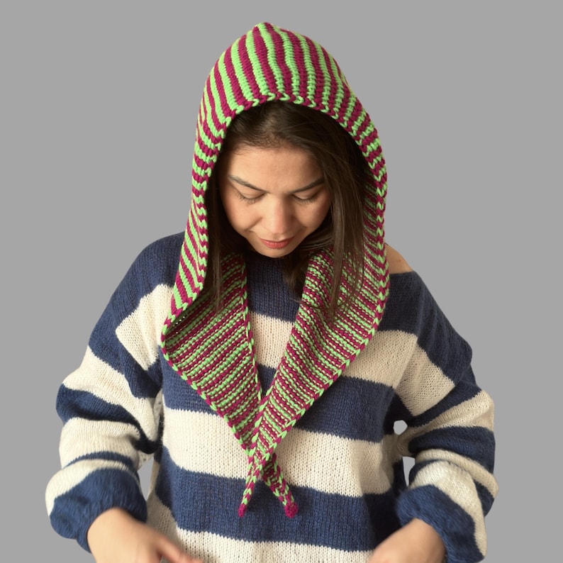 May include: A knitted hood in green and burgundy stripes. The hood is worn over the head and drapes down the front. The person in the image is wearing a blue and white striped sweater.