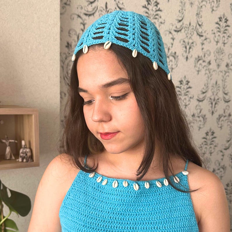 May include: A light blue crochet top with a white crochet hat. Both pieces are decorated with white shell beads.