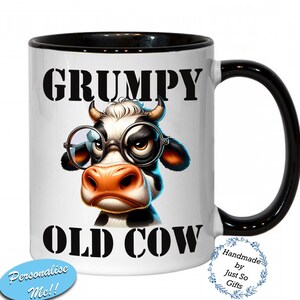 Peut inclure: Mug en céramique blanche avec intérieur et anse noirs. La tasse présente une vache de dessin animé portant des lunettes avec les mots "GRUMPY OLD COW" en lettres noires. Un autocollant ovale bleu dit "Personalise Me!!".