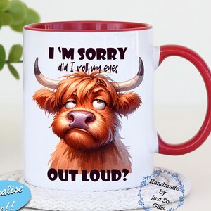Op de afbeelding: Witte keramische mok met een rode binnenkant en handvat. De mok heeft een cartoon illustratie van een Schotse Hooglander met de tekst "I'M SORRY did I roll my eyes OUT LOUD?". De mok staat op een witte onderzetter.