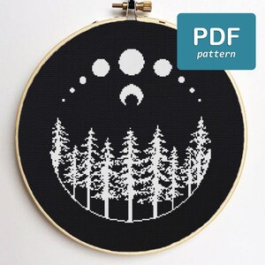 May include: Black and white cross stitch pattern of a crescent moon and stars above a row of pine trees. The pattern is in a round embroidery hoop. The text "PDF pattern" is in a blue box in the upper right corner of the image.