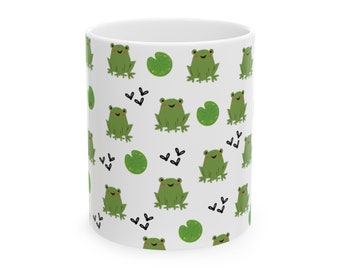 May include: White ceramic mug with a repeating pattern of smiling green frogs, lily pads, and small black accents. The mug is cylindrical and has a glossy finish, suitable for hot or cold drinks.