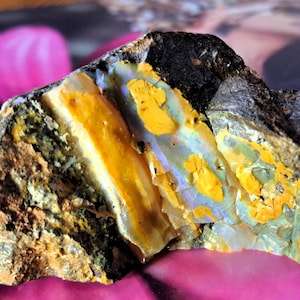 May include: A rough, gray rock with a section of iridescent opal. The opal is a mix of yellow, blue, and green colors.