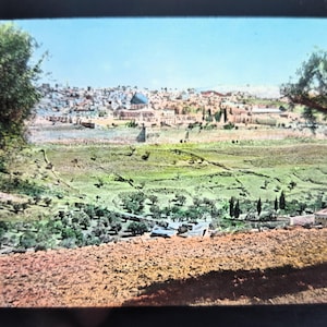 May include: A panoramic view of a city with a large building in the center, surrounded by trees and hills. The city is in the distance, and the hills are in the foreground. The sky is blue and there are clouds in the sky.