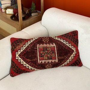 Könnte beinhalten: Ein rotes, weißes und schwarzes Kissen mit geometrischem Muster. Das Kissen liegt auf einem weißen Sofa vor einer orangefarbenen Wand.