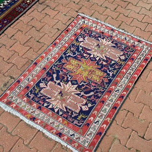 Puede incluir: Una alfombra turca tradicional con un patrón geométrico en tonos rojos, azules, amarillos y blancos. La alfombra tiene un borde con flecos y está colocada sobre una superficie de ladrillo.