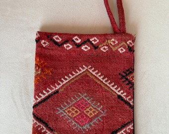 May include: A red fabric clutch with a black handle and a geometric pattern in shades of orange, pink, and gray.