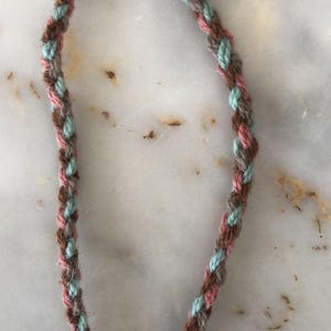 May include: A braided cord with brown, pink, and light blue threads.