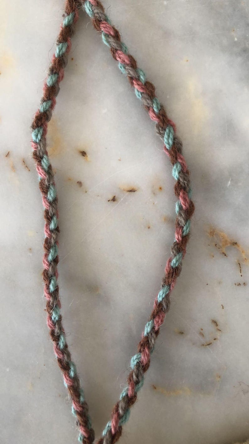 May include: A braided cord with brown, pink, and light blue threads.