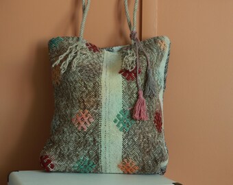 Puede incluir: Un bolso tote tejido con un patrón a rayas marrón, blanco y rosa. El bolso tiene un diseño geométrico con detalles coloridos y borlas.