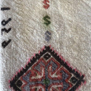 May include: A white fabric with a black and red embroidered design. The design is a diamond shape with a floral pattern in the center. The fabric has the number "1978" written on it in black thread.