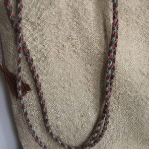 May include: A beige tote bag with two braided straps. The straps are made of brown, pink, and blue yarn.