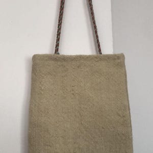 May include: A beige tote bag with a woven texture and two long straps made of brown and blue rope.