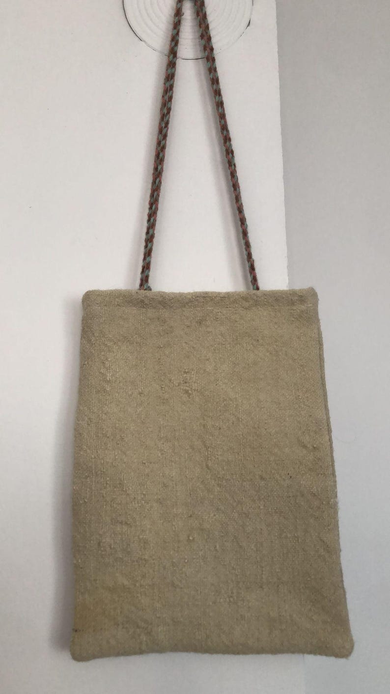 May include: A beige tote bag with a woven texture and two long straps made of brown and blue rope.