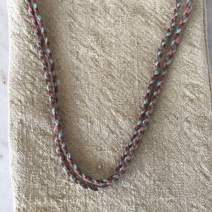 May include: A beige linen tote bag with a braided strap made of brown, pink, and blue yarn.