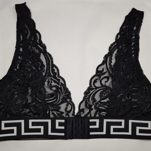 May include: Black lace bralette with a V-neck design. The bralette features a decorative white and black geometric pattern along the bottom band. The bra has adjustable straps and a hook-and-eye closure in the back.